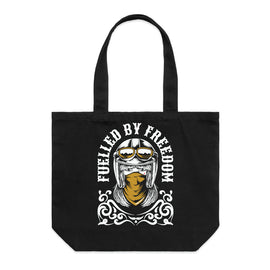 A black canvas tote bag with two top handles, featuring a graphic print of a helmeted motorcycle rider with goggles and the text 'FUELLED BY FREEDOM' in white.