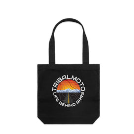circle design includes the words TribalMoto and Life Behind Bars with a sunset, mountains and a road. Layered with topographical lines on black tote