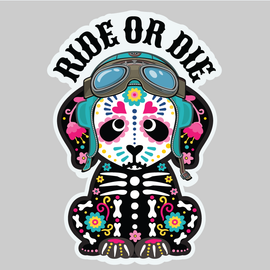 A die-cut sticker featuring a cartoon dog styled with Day of the Dead sugar skull makeup, wearing aviator goggles and a skeleton-print jacket, beneath the text 'RIDE OR DIE' in black arched letters, shown on a solid gray background.