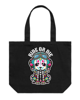 A black canvas tote bag with two handles, featuring a colorful graphic of a seated skeleton wearing motorbike helmet and goggles and the words 'RIDE OR DIE' printed above it, shown against a plain white background.