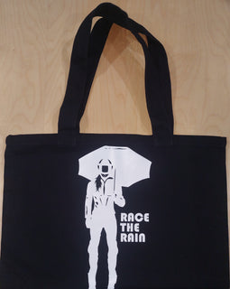 Black tote bag with design of lady motorbike rider holding umbrella and words Race the rain