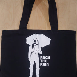 Black tote bag with design of lady motorbike rider holding umbrella and words Race the rain